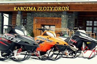One orange and two black snowmobiles in fornt of entrance to hotel s inn